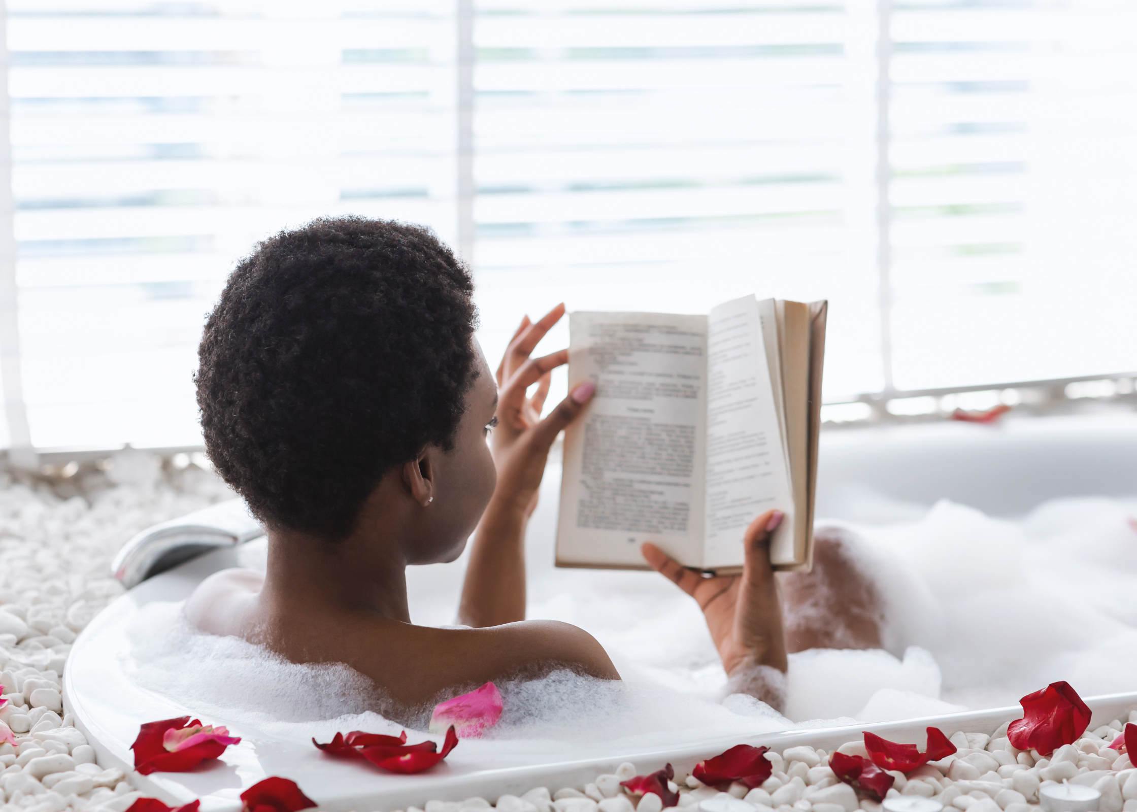 black woman sitting in a bubble bath reading a book with rose petals around the bath. how to take time for yourself. self care ideas for mind body and soul. self-care ideas for mental health. me time ideas