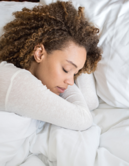 mixed race black woman with curly hair sleeping napping on white bedding and sheets. nighttime routine ideas. evening routine ritual. bedtime routine checklist. nighttime skincare routines. Tips for better sleep