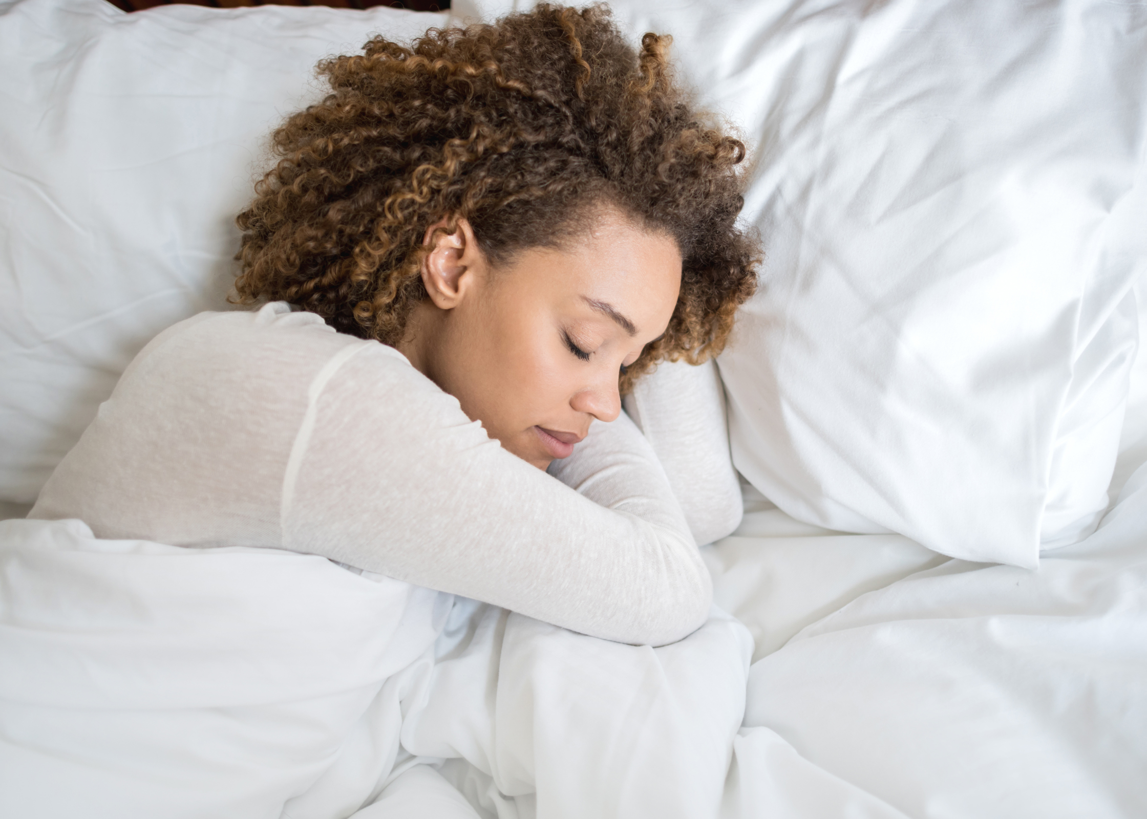 mixed race black woman with curly hair sleeping napping on white bedding and sheets. nighttime routine ideas. evening routine ritual. bedtime routine checklist. nighttime skincare routines. Tips for better sleep