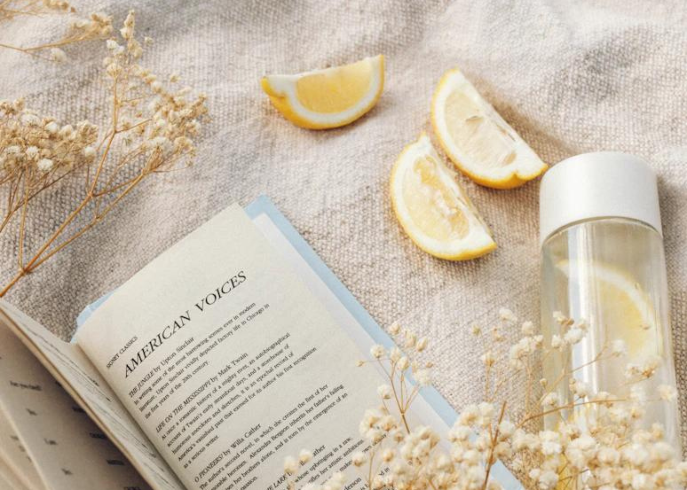 lemon infused water in bottle with lemons and a book against a blanket. selfcare ideas for the summer. Summer self-care ideas, health and wellness tips for the summer. the best summer check list. Get summer ready